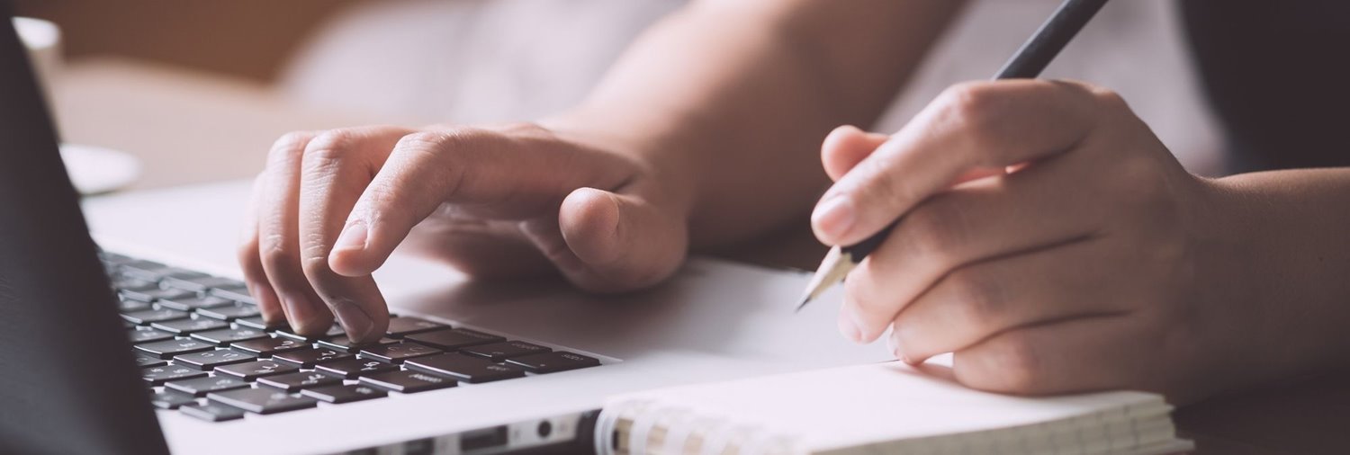 person taking notes while looking at computer