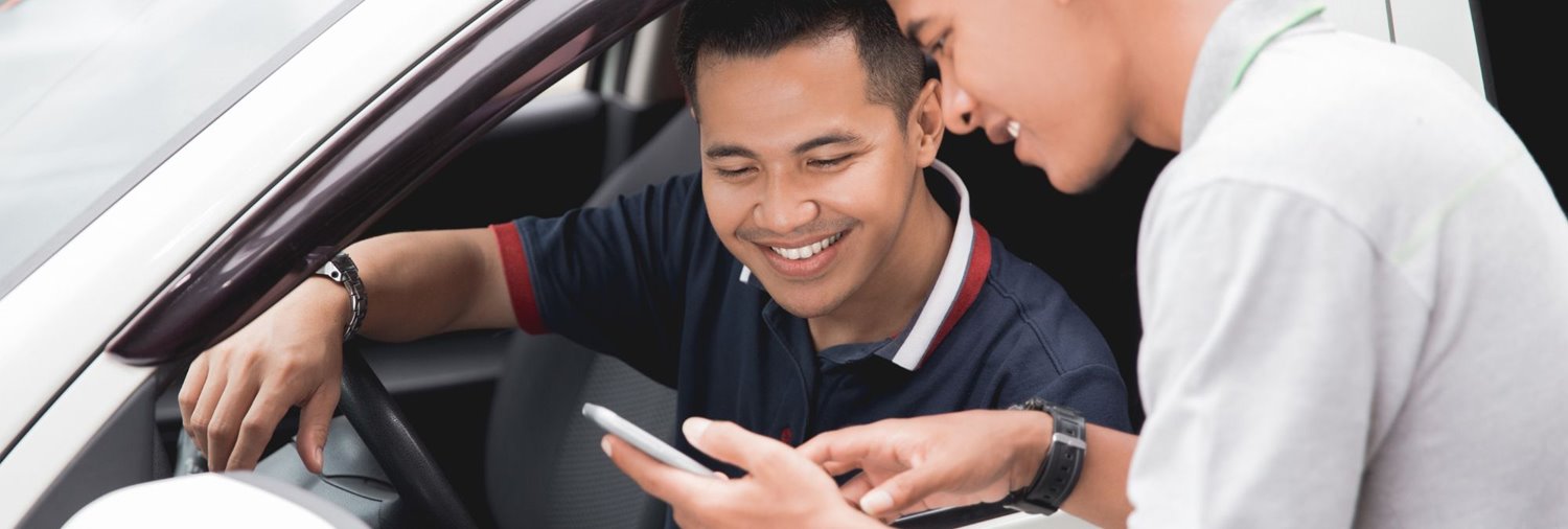 male holding mobile phone and showing it to a man in a white vehicle