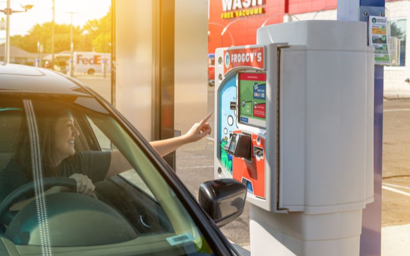smiling woman in a car reaching out to a car wash pay station touchscreen
