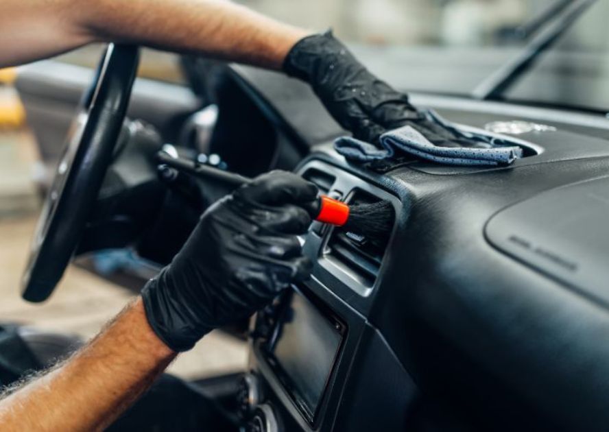 gloved hands brushing out a car air vent at a full service car wash
