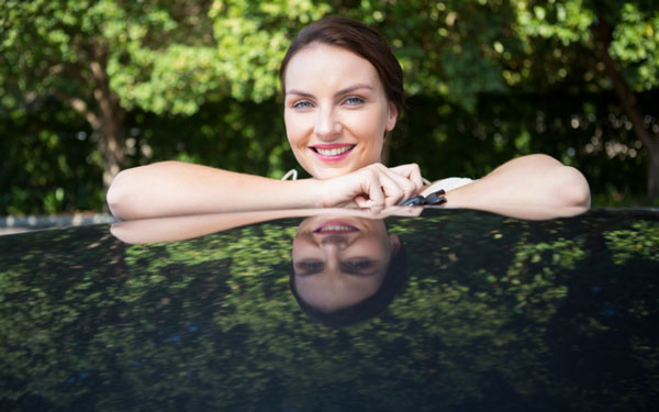 A Burnette woman with her arms folded on top of a black car smiling