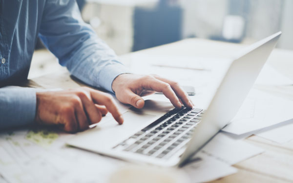 man in blue shirt typing on a laptop 