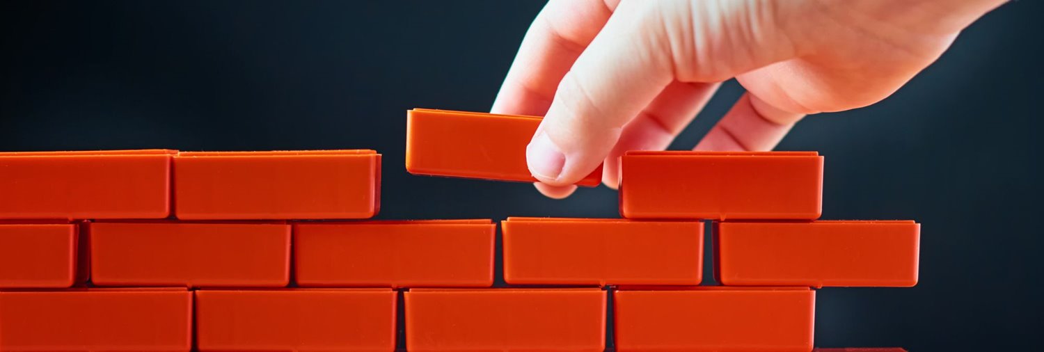 hand setting a red block on a wall of other red blocks