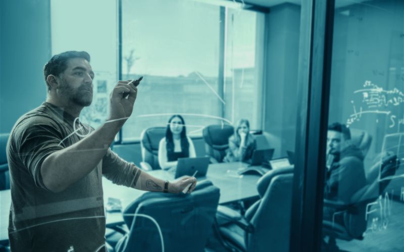 SUDS staff member writing on the glass of a conference room wall while colleagues watch in the background