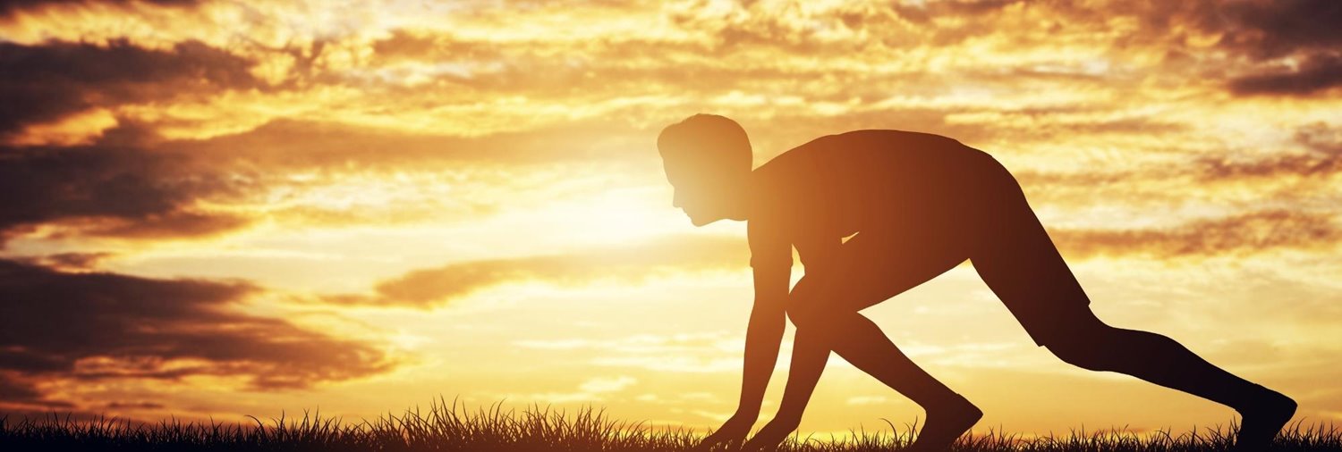 man crouched down as if he's about to start a race in the sunrise
