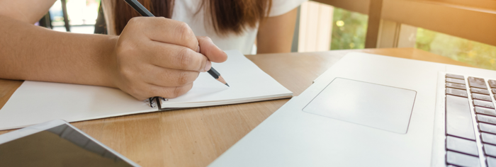 woman writing in a notebook beside a laptop